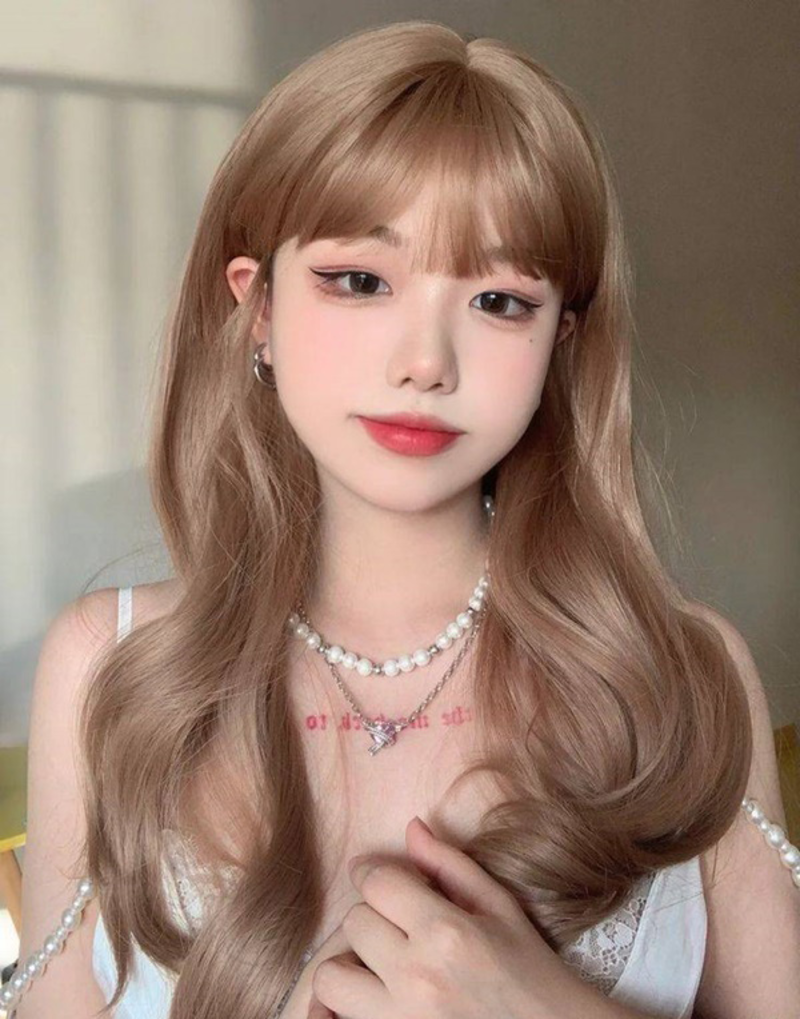 toc-uon-mai-bang-1 Người có mái tóc dài màu nâu, trang điểm nhẹ, đeo vòng cổ ngọc trai, mặc áo trắng có dây.