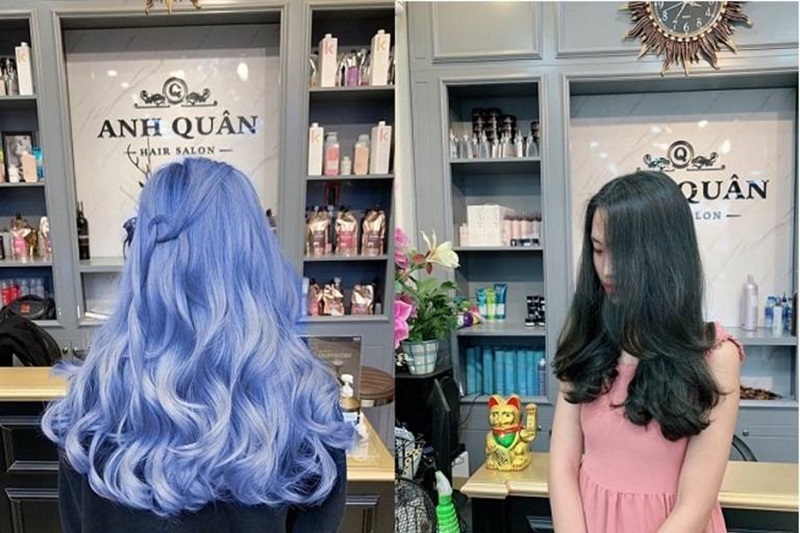 Hai người đang đứng trước gương tại một tiệm làm tóc, một người tóc xanh, người kia tóc đen, xung quanh là kệ sản phẩm.