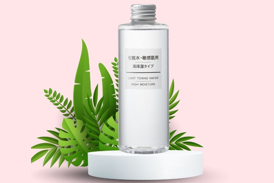 Chai nước hoa hồng trong suốt đặt trên nền màu hồng, xung quanh là lá cây xanh.