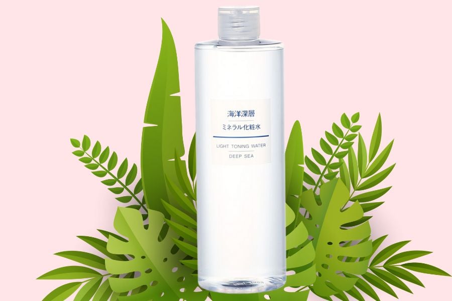 Chai nước hoa hồng trong suốt, nền hồng, xung quanh trang trí bằng lá cây xanh.
