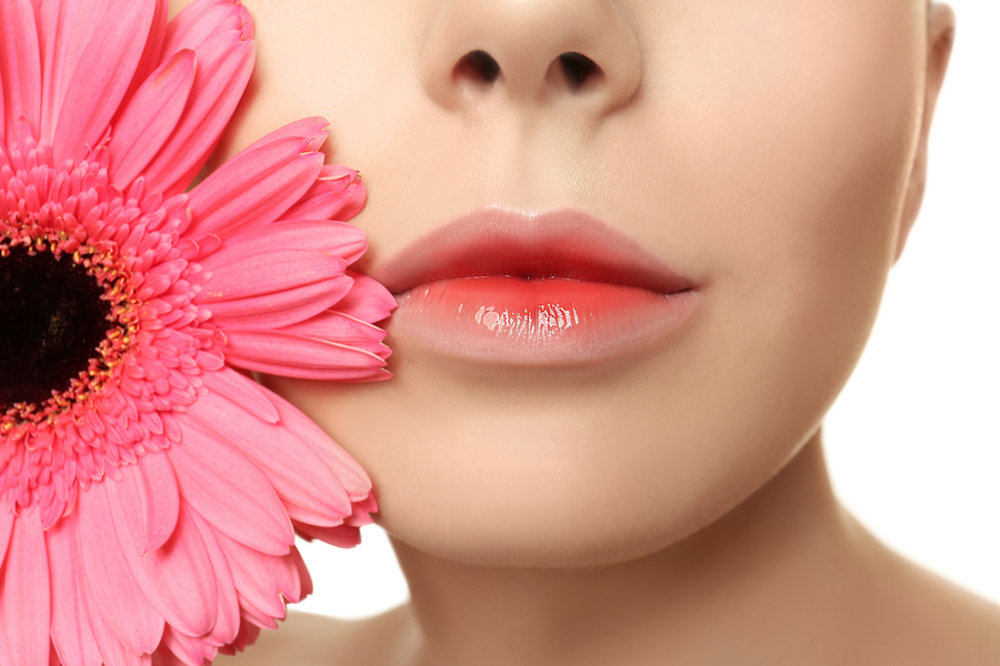 Cận cảnh môi hồng bóng và hoa cúc màu hồng bên má trên nền trắng.