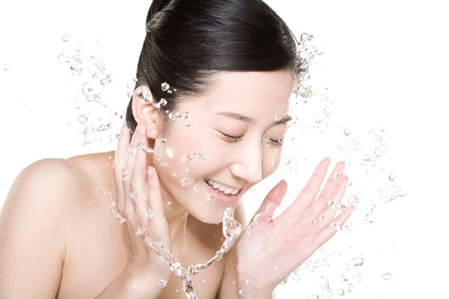 Người đang tươi cười, rửa mặt bằng nước, với bọt nước bắn tung tóe xung quanh.