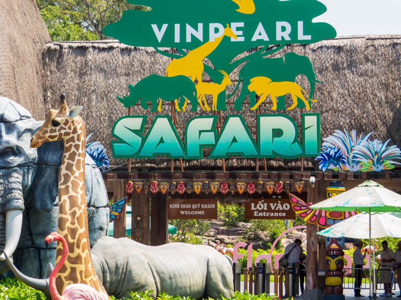 03c48623-tet-nen-di-du-lich-o-dau-02 Lối vào khu safari với biển hiệu lớn và mô hình động vật trang trí xung quanh, có khách du lịch tham quan.