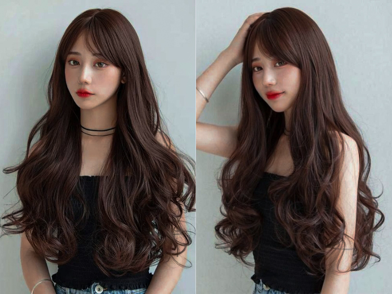 Người phụ nữ với mái tóc dài, xoăn, màu nâu, mặc trang phục đen, đứng trước phông nền màu xám.