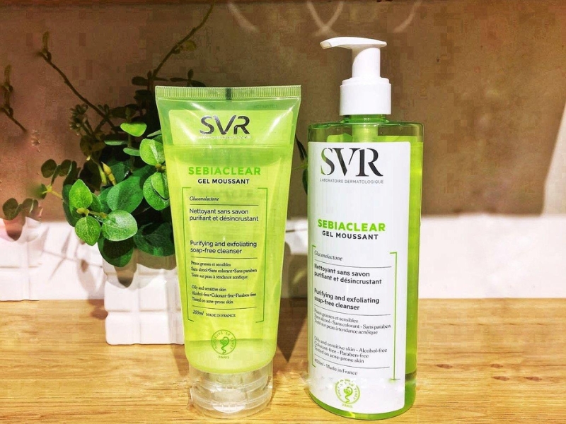 09e4976c-sua-rua-mat-cho-da-dau-16 Hai chai gel rửa mặt SVR Sebiaclear trên bàn gỗ, nền có cây xanh trang trí.