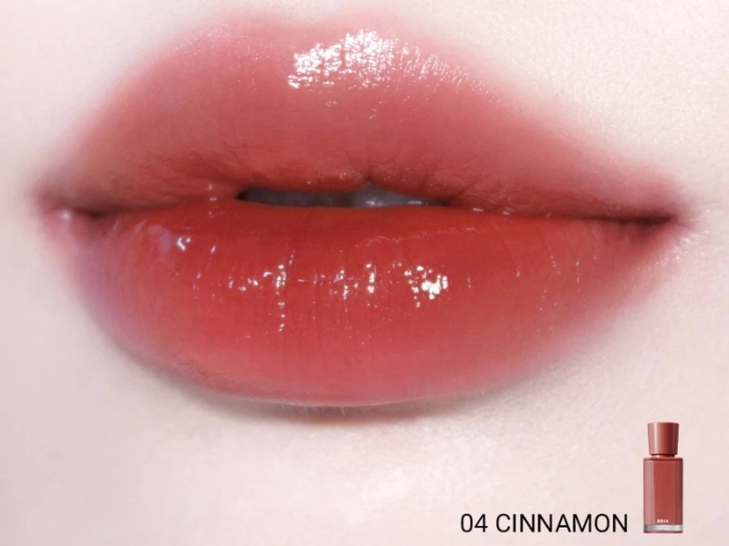 Đôi môi với son bóng màu đỏ nâu, phía dưới có một chai son nhỏ cùng dòng chữ "04 CINNAMON".