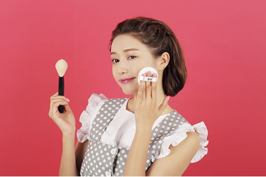Người cầm cọ trang điểm và hộp phấn, nền màu hồng.