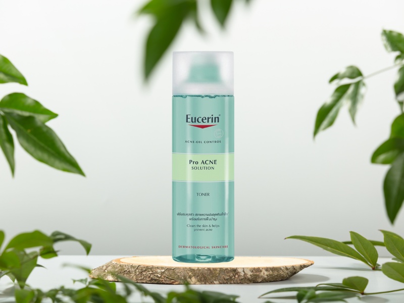 Chai toner màu xanh lá cây nhãn hiệu Eucerin, đặt trên mặt gỗ, xung quanh có lá cây xanh.