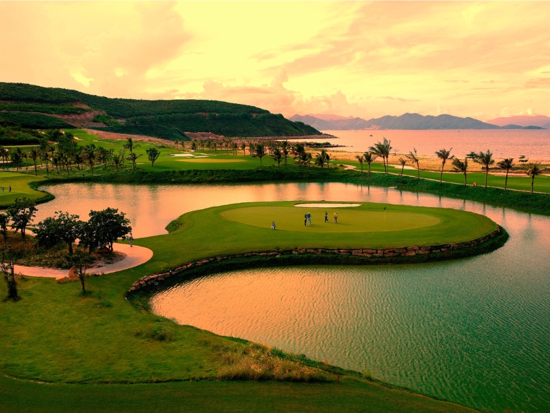 1c52ad97-tet-nen-di-du-lich-o-dau-03 Sân golf xanh tươi với hồ nước và núi non bao quanh, cảnh hoàng hôn tạo nên bầu không khí yên bình và thơ mộng.