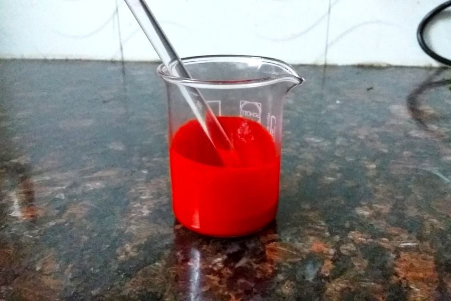 Ống đong chứa dung dịch màu đỏ trên bề mặt đá cẩm thạch, có ống khuấy thủy tinh bên trong.