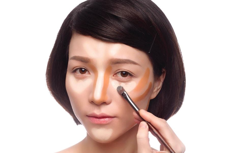 Người đang được trang điểm với các vùng sáng tối trên mặt, sử dụng cọ để tán đều phấn.