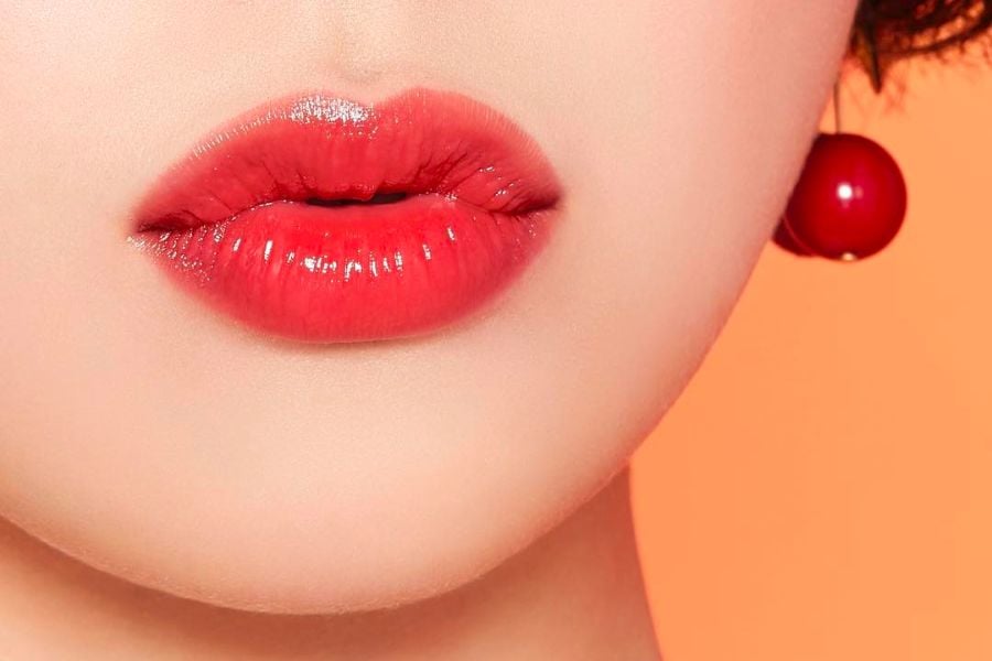 Đôi môi được tô son đỏ bóng, bên cạnh là khuyên tai màu đỏ, nền phía sau màu cam nhạt.