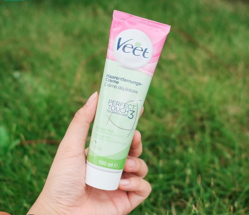 21c4b795-review-kem-tay-long-veet-41 Người cầm tuýp kem tẩy lông màu hồng và xanh, nền cỏ xanh phía sau.