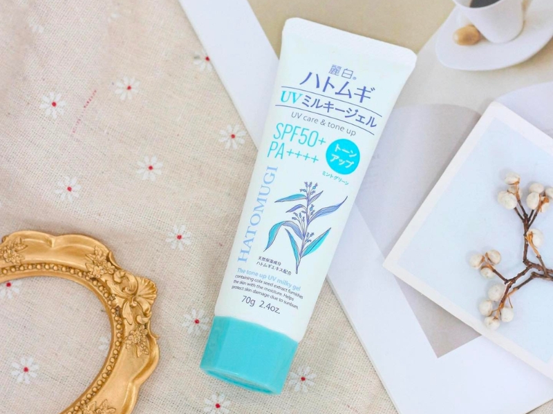 2244b889-kem-chong-nang-hatomugi-co-may-loai-11 Tuýp kem chống nắng SPF50+ nằm trên bàn, cạnh khung ảnh nhỏ và cành hoa khô.