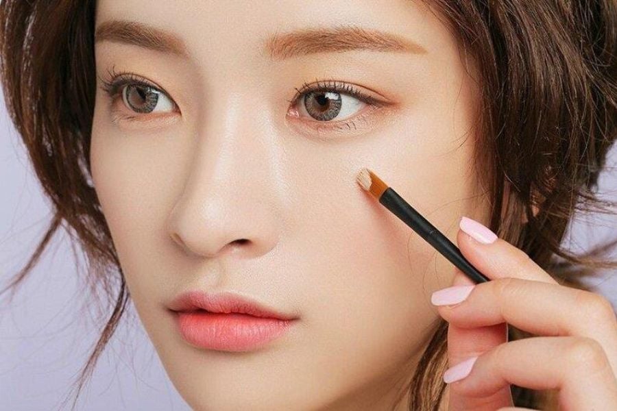 Người cầm cọ trang điểm gần mắt, chuẩn bị thoa phấn lên vùng da quanh mắt.