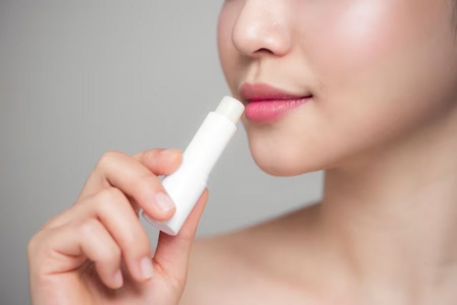 Người cầm thỏi son dưỡng môi gần miệng, chuẩn bị thoa lên môi.