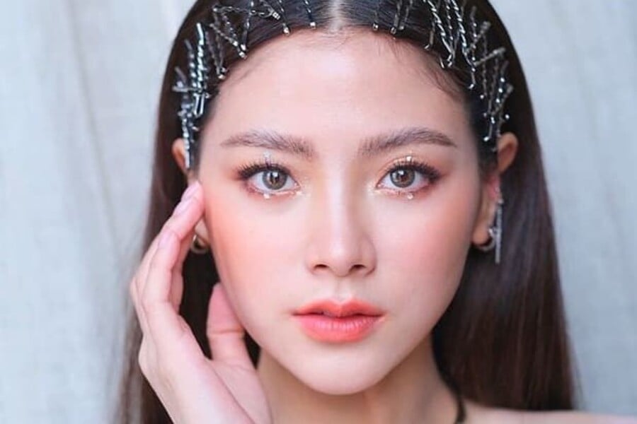 Người phụ nữ trang điểm nhẹ, tóc thẳng, đeo phụ kiện tóc lấp lánh, nhìn thẳng vào máy ảnh.