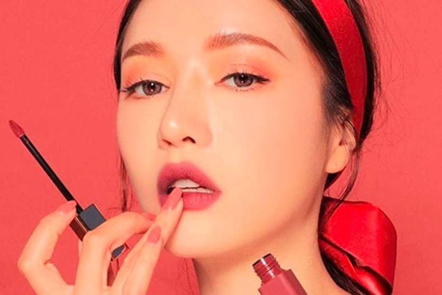 Người phụ nữ trang điểm với son môi đỏ, đeo băng đô đỏ, trên nền màu đỏ.