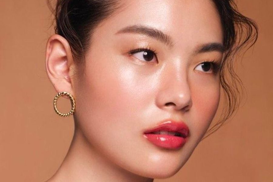 Cận cảnh gương mặt một người với trang điểm tự nhiên, đôi môi đỏ, và đeo bông tai tròn vàng.