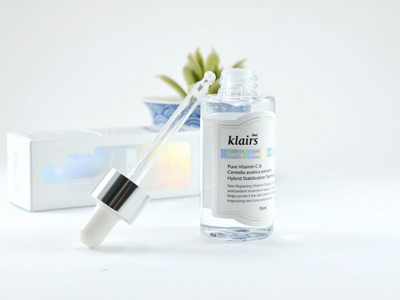 301ae08f-serum-lam-deu-mau-da-5 Chai serum với ống nhỏ giọt đặt trên bàn, phía sau có hộp giấy và một chậu cây nhỏ.