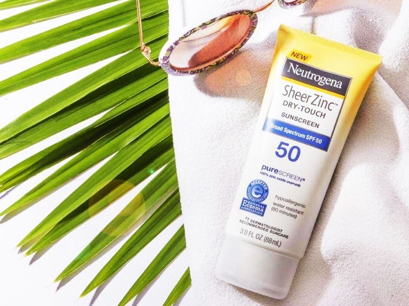 Kem chống nắng SPF 50 cùng kính mát và lá cọ trên nền vải trắng.