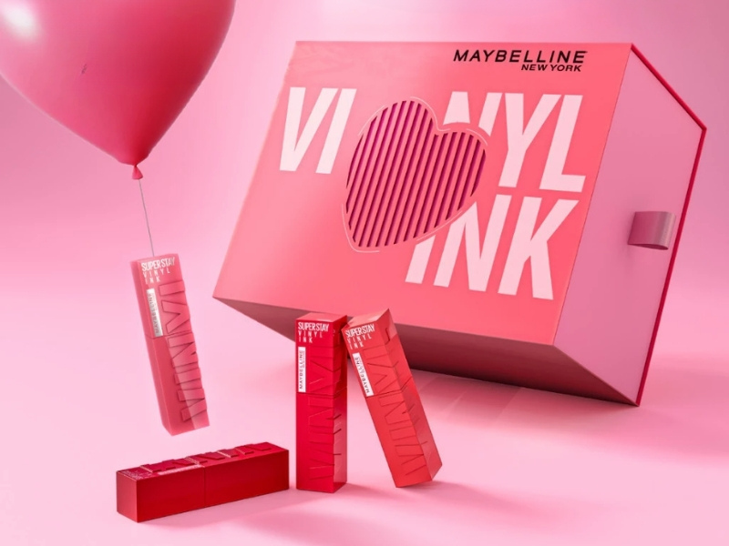 3bc2443e-review-son-maybelline-12 Hộp quà màu hồng với chữ "Vinyl Ink", kèm son và bóng bay, trên nền màu hồng.