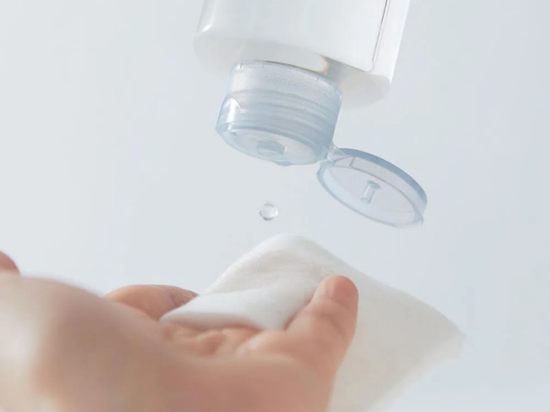 Bàn tay cầm miếng bông, chai mỹ phẩm đang nhỏ giọt chất lỏng xuống.