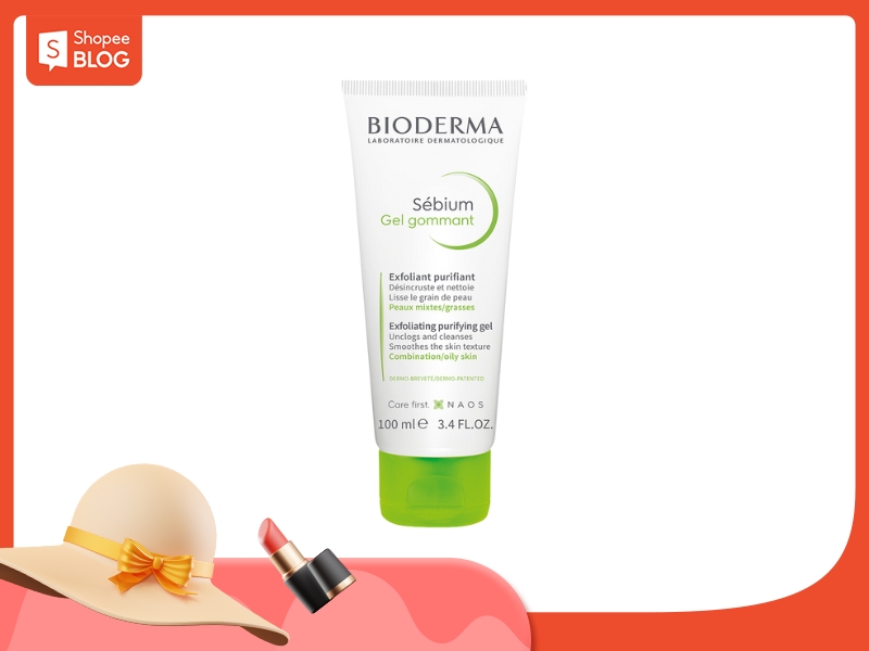 Tuýp gel tẩy tế bào chết Bioderma Sébium 100ml, nắp màu xanh lá, trên nền đỏ với hình mũ và son môi.