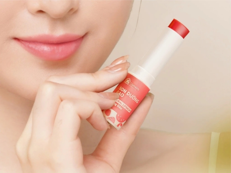 Người cầm một thỏi son dưỡng môi màu đỏ, gần khuôn mặt với đôi môi hồng tự nhiên.
