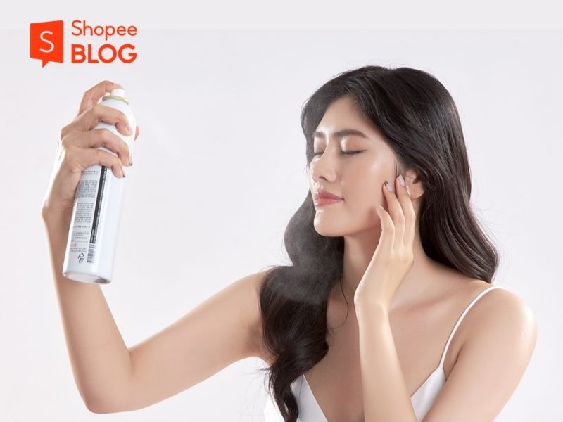 Người phụ nữ đang xịt khoáng lên mặt, mắt nhắm, tay cầm bình xịt. Logo Shopee Blog ở góc trên trái.