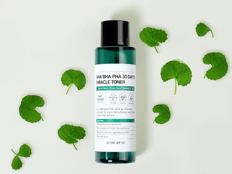 Chai toner màu xanh lá cây, nhãn trắng, nằm trên nền trắng kèm các lá cây xanh xung quanh.