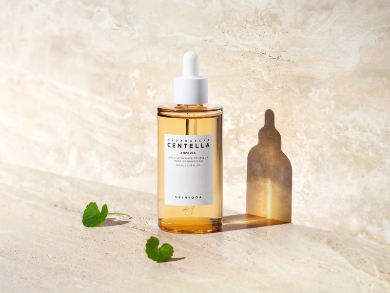 5c17e73e-serum-cho-da-hon-hop-thien-dau-8 Chai serum với nhãn "Centella", nắp nhỏ giọt màu trắng, đặt trên nền đá cẩm thạch, cạnh lá xanh.