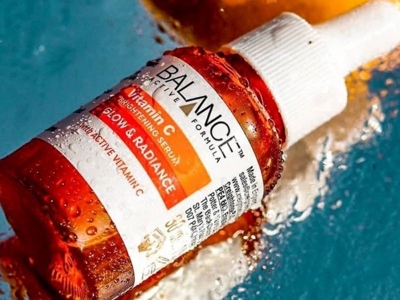 5ee72943-serum-lam-deu-mau-da-3 Chai serum màu cam với nhãn Vitamin C, nằm trên bề mặt nước, có những giọt nước đọng trên bề mặt.
