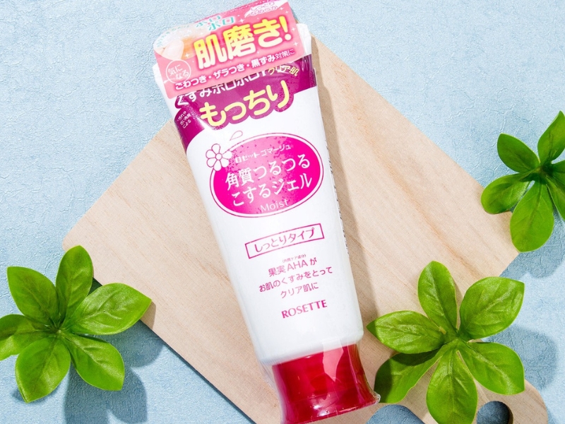 5f1124e0-hasaki Tuýp kem dưỡng ẩm màu trắng có nắp đỏ, đặt trên nền xanh, xung quanh có lá cây xanh.