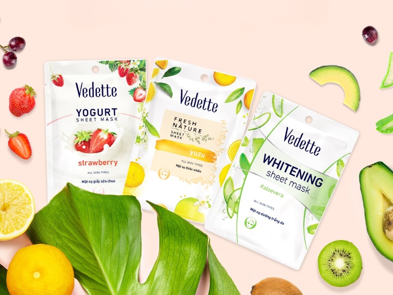 Ba gói mặt nạ giấy Vedette với các thành phần dâu, yuzu và nha đam trên nền trái cây và lá xanh.