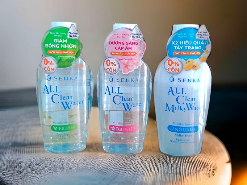 869c3e60-nuoc-tay-trang-senka-co-tot-khong-1 Ba chai nước tẩy trang Senka All Clear Water trên bàn gỗ, với các đặc tính khác nhau được ghi trên nhãn.