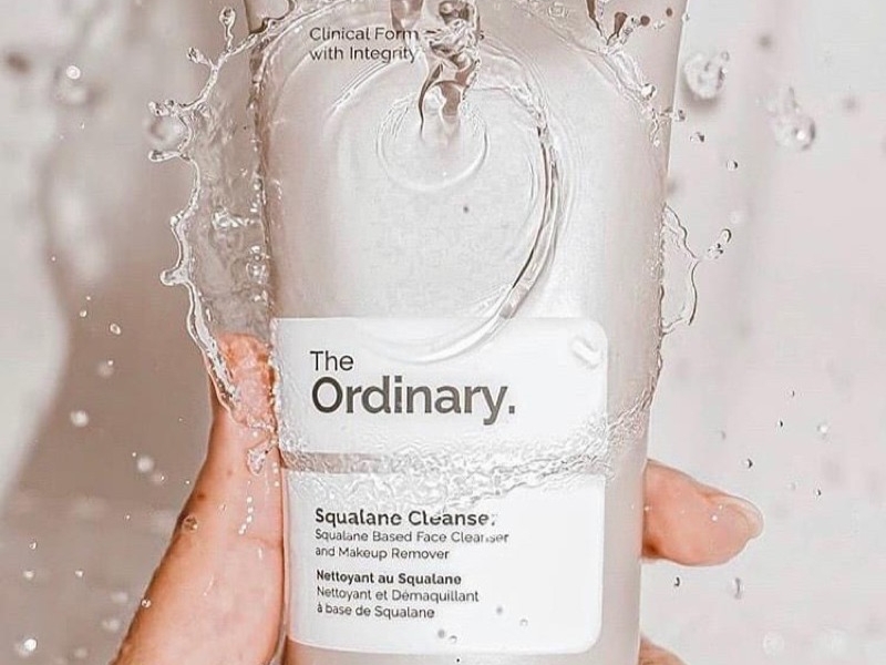 8a8776a1-sua-rua-mat-tay-trang-6 Chai sữa rửa mặt The Ordinary Squalane Cleanser được cầm trên tay, nước bắn tung tóe xung quanh.