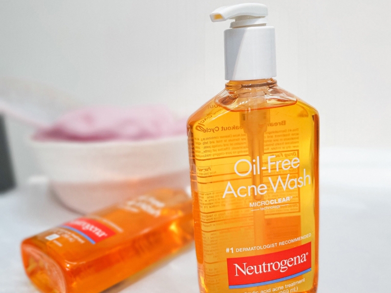 9c6aaac1-sua-rua-mat-cho-da-dau-07 Chai sữa rửa mặt màu cam với nhãn "Oil-Free Acne Wash" đặt trên bề mặt trắng.