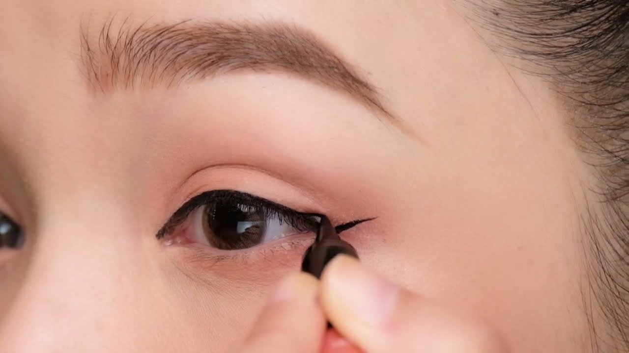 Bí Quyết Tạo Điểm Nhấn: Xu Hướng Trang Điểm Đính Đá Ở Mắt 3 Người đang kẻ mắt bằng bút kẻ mắt màu đen, tạo đường viền sắc nét trên mí mắt trên.