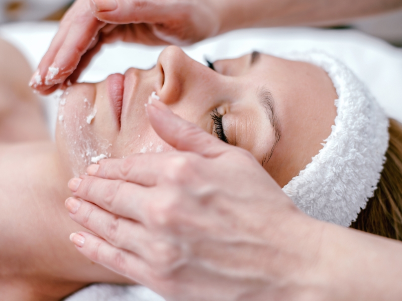 Người phụ nữ đang được mát-xa mặt với sản phẩm dưỡng da, nằm thư giãn trên giường spa.