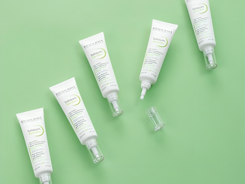 a24860b8-kem-duong-am-bioderma-cho-da-dau-mun-9 Các tuýp kem dưỡng da màu trắng nằm trên nền xanh lá, một số có nắp đậy, một số không.