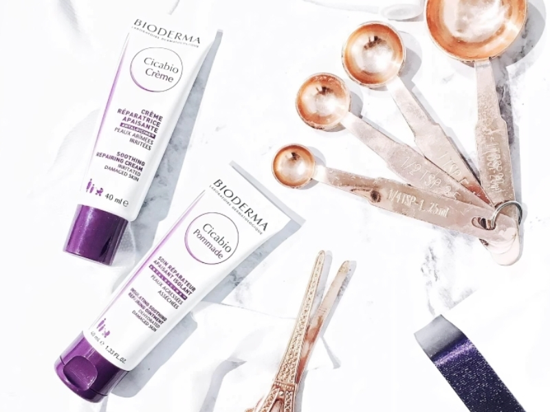 a5b37fbb-kem-duong-am-bioderma-cho-da-dau-mun-5 Hai tuýp kem dưỡng da Bioderma Cicabio và bộ thìa đong kim loại trên nền trắng.