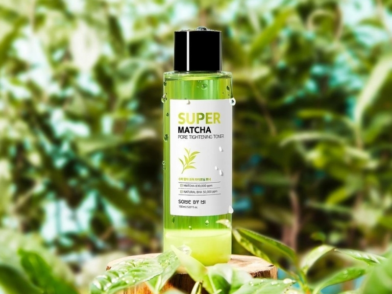 aa5130fe-toner-cho-da-thuong-3 Chai toner màu xanh lá cây, nhãn hiệu "Super Matcha", đặt trên nền lá cây xanh.