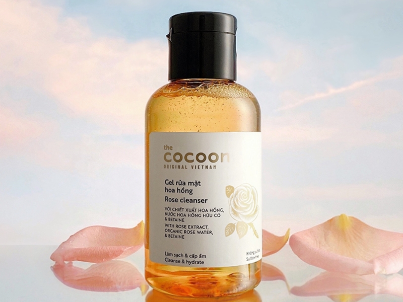 af7587a6-sua-rua-mat-cho-da-hon-hop-thien-kho-15 Chai gel rửa mặt hoa hồng với nhãn hiệu, đặt trên nền trời xanh và cánh hoa hồng.