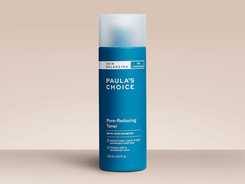 Chai toner màu xanh dương đậm, tên thương hiệu và thông tin sản phẩm in trên nhãn, đặt trên nền màu be.