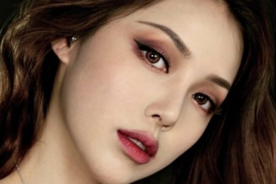 Cận cảnh khuôn mặt với trang điểm mắt sắc nét và đôi môi hồng, tóc nâu dài xõa tự nhiên.