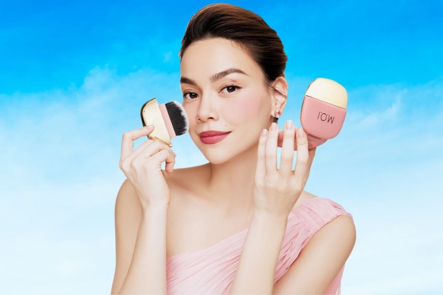 Người phụ nữ cầm cọ trang điểm và thiết bị chăm sóc da trên nền trời xanh.