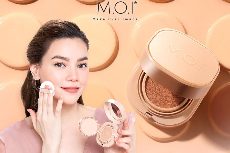 Người phụ nữ dùng phấn nước M.O.I, nền phông màu be với hộp phấn trang điểm bên cạnh.