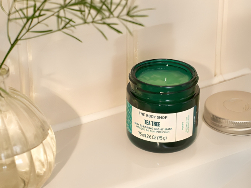 c146e2ef-review-mat-na-ngu-12 Hũ mặt nạ tràm trà trên kệ, cạnh lọ cây nhỏ, nắp để bên cạnh.