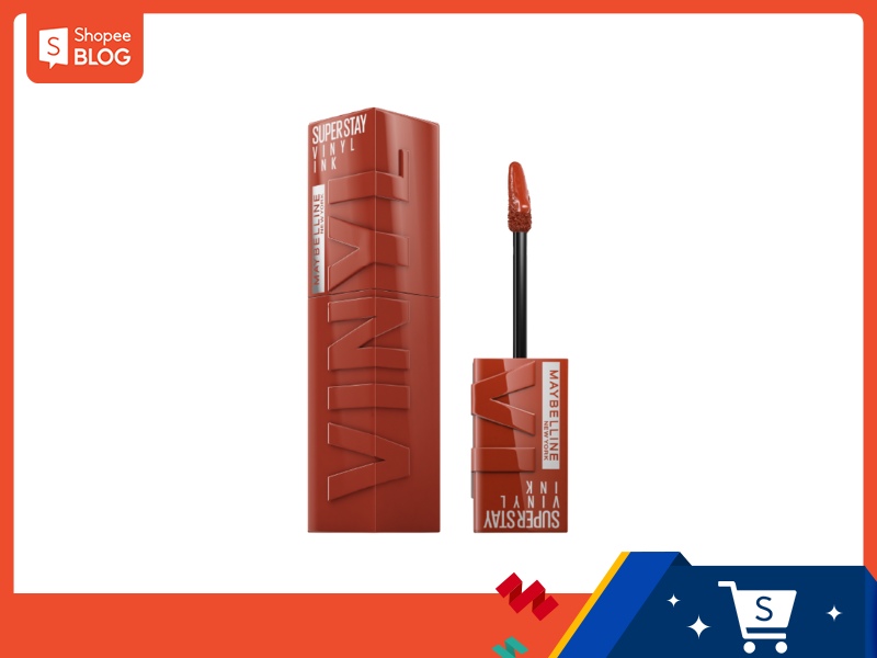 c28f61a1-review-son-maybelline-16 Son môi màu đỏ cam với cọ, hộp chữ nhật đứng, nền trắng, viền trang trí màu cam.